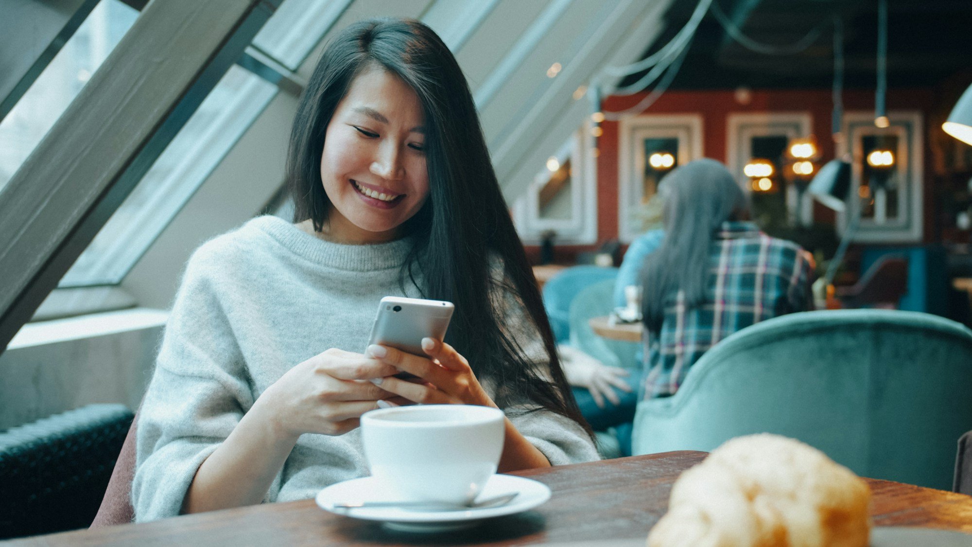Frau im Café schaut lächelnd auf ihr Smartphone